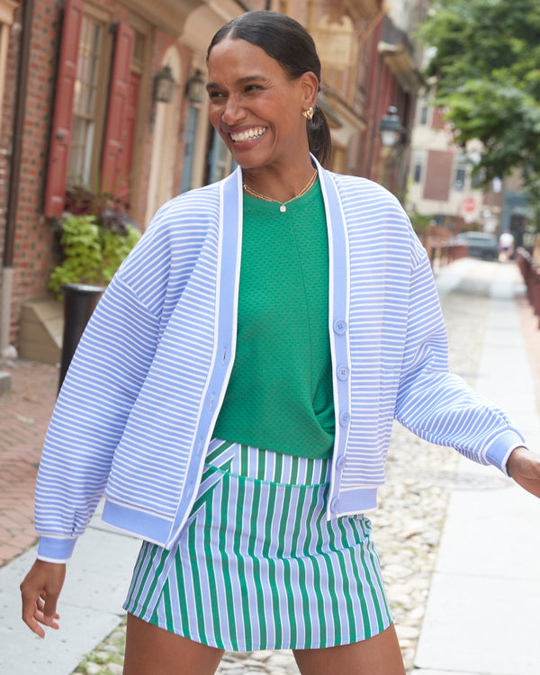 Model is wearing the abbott sweatshirt cardigan in violet stripe paired with everyday skort in violet/evergreen stripe and topspin tank in evergreen