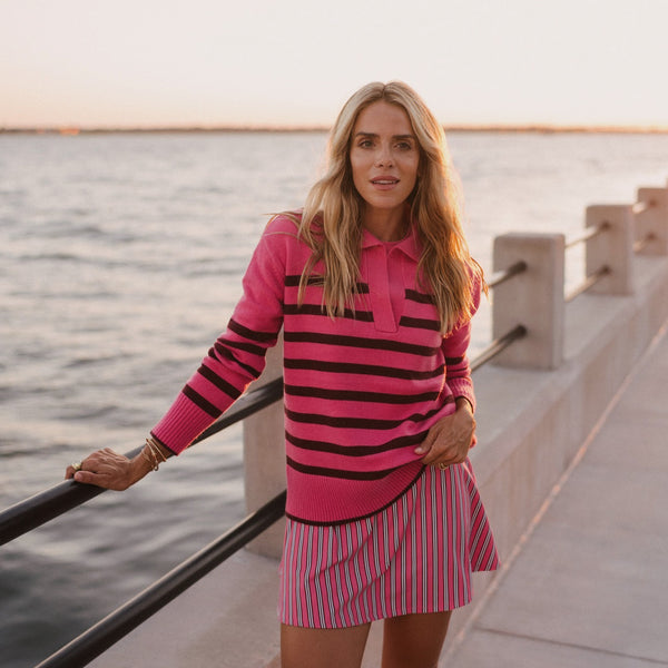 Model is wearing the Carlyle rugby sweater in rose/ lacquer stripe paired with the pounce skort in rose/ lacquer triple stripe. 