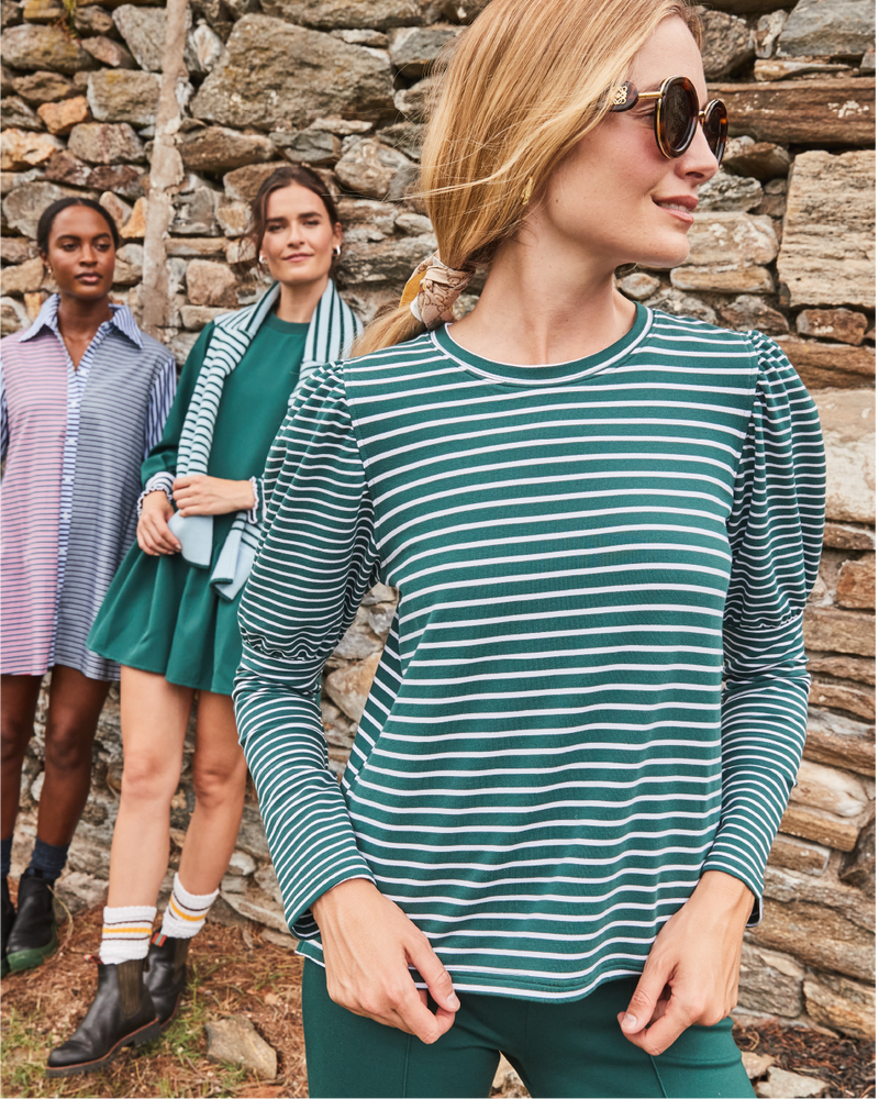 Model right is wearing the Webster Top in Ivy/ Super White Stripe with the Waverly Pants in Ivy. Model Center is wearing the Vine Dress in Ivy with the Carlyle Crewneck in Baby Blue/ Ivy Stripes around her shoulders. Model left is wearing the Bloom Shirt Dress in Navy/ Cherry Stripes.