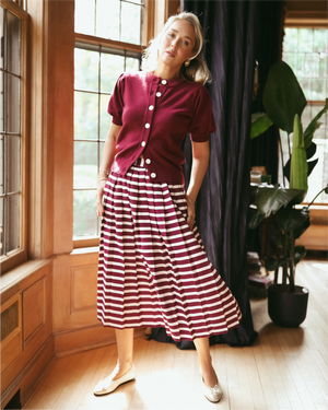 Mary Orton is wearing the Gigi Cardigan in Burgundy with the Liza Skirt in Burgundy/ Ivory Stripe.