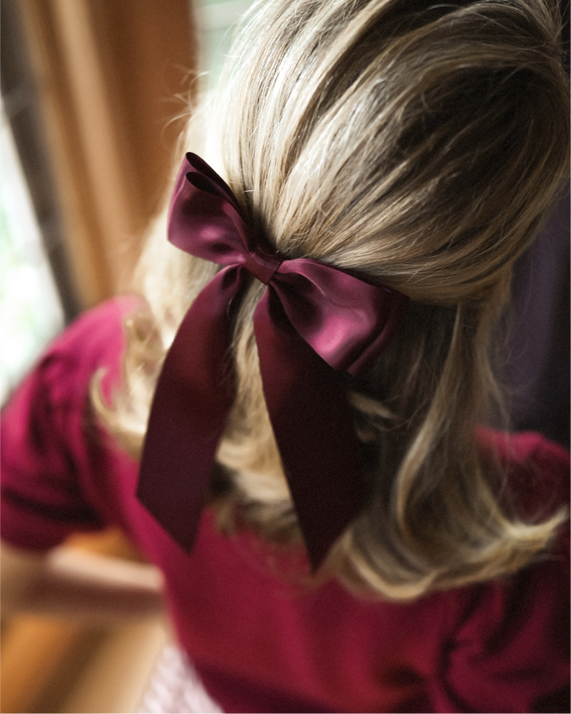 Mary Orton is wearing the GIgi Cardigan in Burgundy with the Charlotte Bow in Burgundy in her hair.
