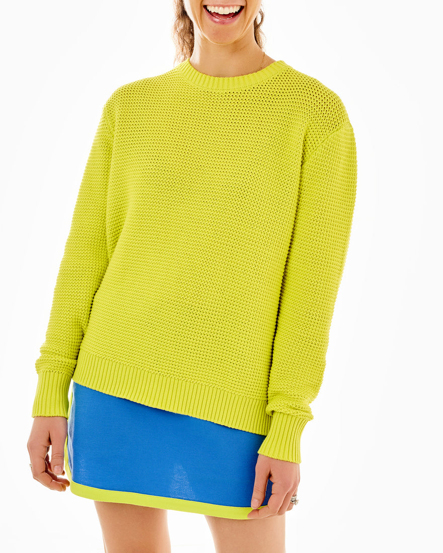 Model is wearing the open knit match point sweater in chartreuse paired with the textured pique Lennon skort in cerulean/chartreuse. 