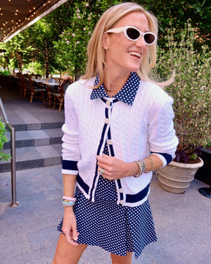 Model is wearing sleeveless virginian polo in navy dottie paired with virginian pleated skort in navy dottie and oxford cardigan in navy/super white